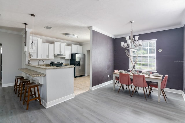 kitchen featuring kitchen peninsula, decorative light fixtures, white cabinetry, appliances with stainless steel finishes, and light wood-type flooring