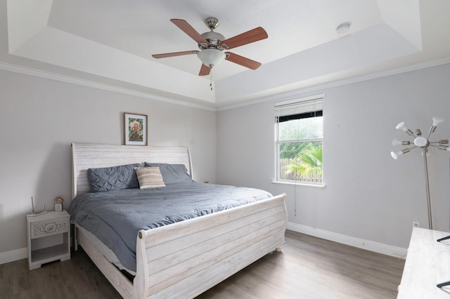 bedroom with ornamental molding, a tray ceiling, dark hardwood / wood-style floors, and ceiling fan