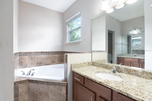 bathroom featuring vanity, toilet, and a relaxing tiled tub