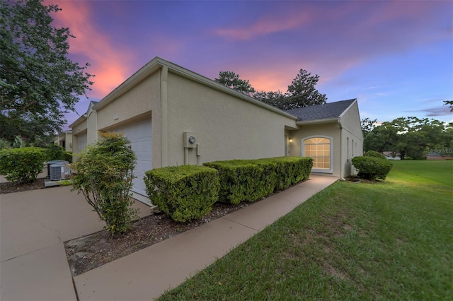 property exterior at dusk featuring a garage, a yard, and cooling unit