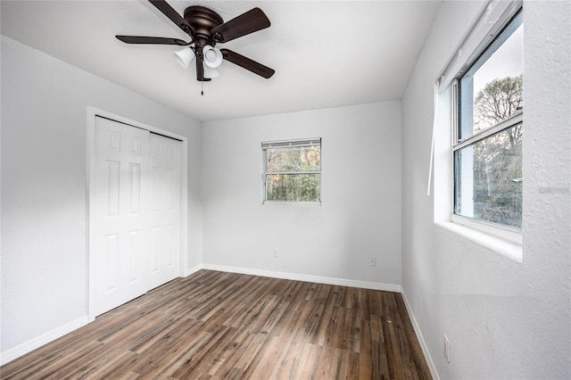 unfurnished bedroom with ceiling fan, dark hardwood / wood-style floors, multiple windows, and a closet