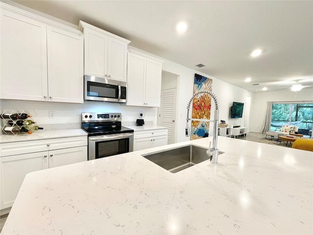 kitchen with sink, light stone countertops, white cabinets, and appliances with stainless steel finishes