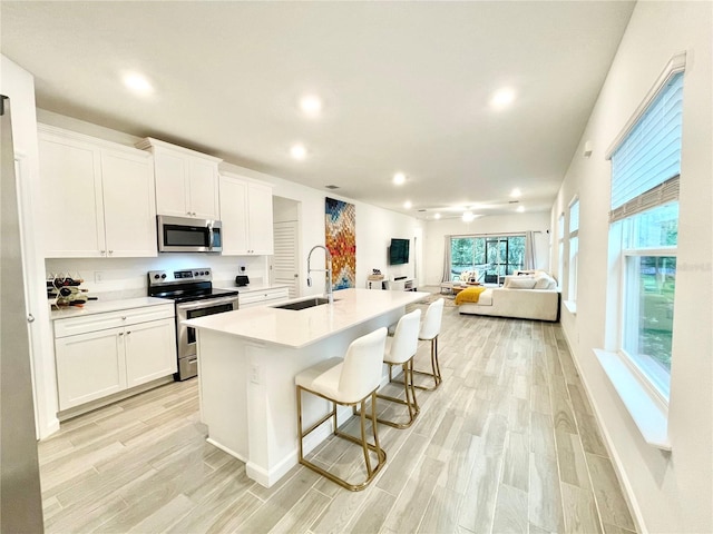 kitchen with stainless steel appliances, white cabinetry, a kitchen island with sink, and sink