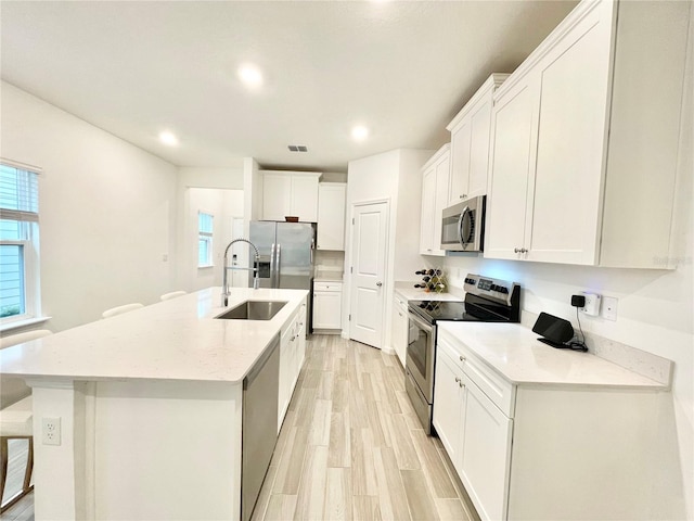 kitchen featuring white cabinetry, sink, stainless steel appliances, and an island with sink