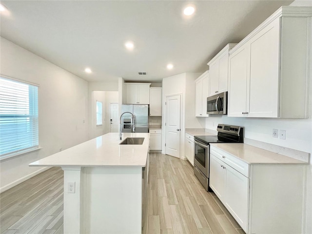 kitchen with stainless steel appliances, a center island with sink, white cabinets, and light hardwood / wood-style floors