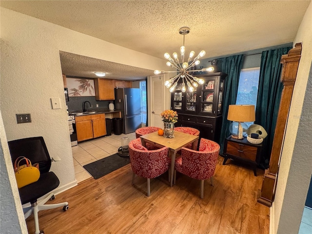 dining area with an inviting chandelier, light hardwood / wood-style floors, sink, and a textured ceiling