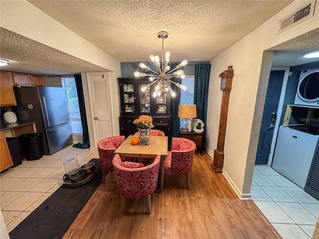 dining area with stacked washer and dryer, a chandelier, light tile patterned floors, and a textured ceiling