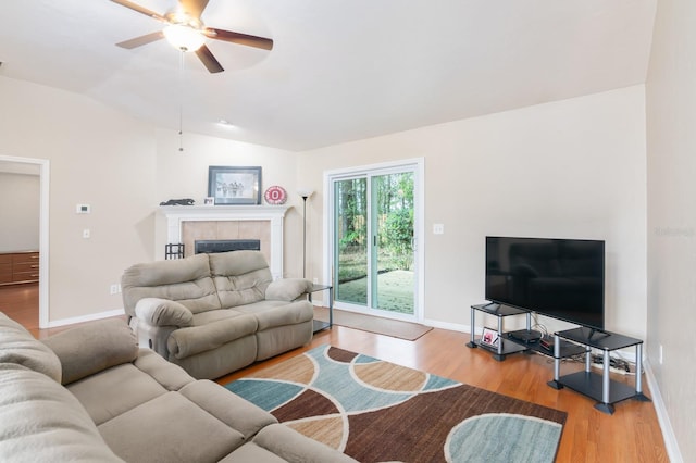 living room featuring hardwood / wood-style floors, a tiled fireplace, ceiling fan, and vaulted ceiling