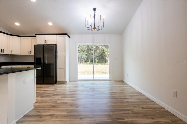 kitchen with light wood-type flooring, white cabinets, black refrigerator with ice dispenser, pendant lighting, and a chandelier