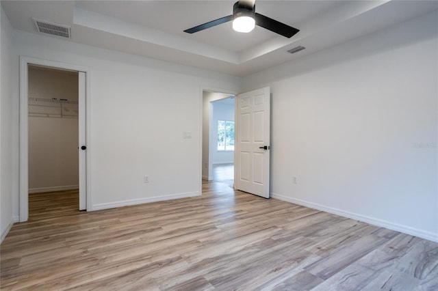 unfurnished bedroom featuring ceiling fan, light wood-type flooring, a closet, and a walk in closet