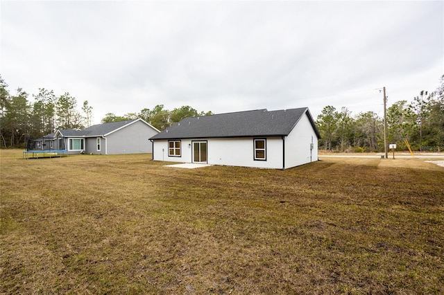 back of house with a trampoline and a lawn