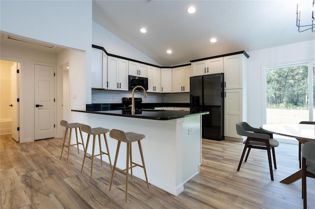 kitchen featuring black fridge, light hardwood / wood-style floors, vaulted ceiling, white cabinetry, and a kitchen bar