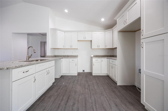 kitchen with light stone counters, dark wood-type flooring, a sink, white cabinetry, and vaulted ceiling