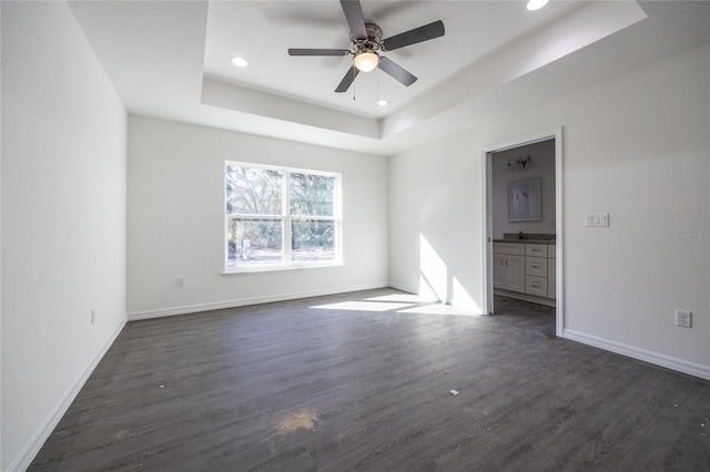 unfurnished bedroom with baseboards, ensuite bath, dark wood-type flooring, a tray ceiling, and recessed lighting