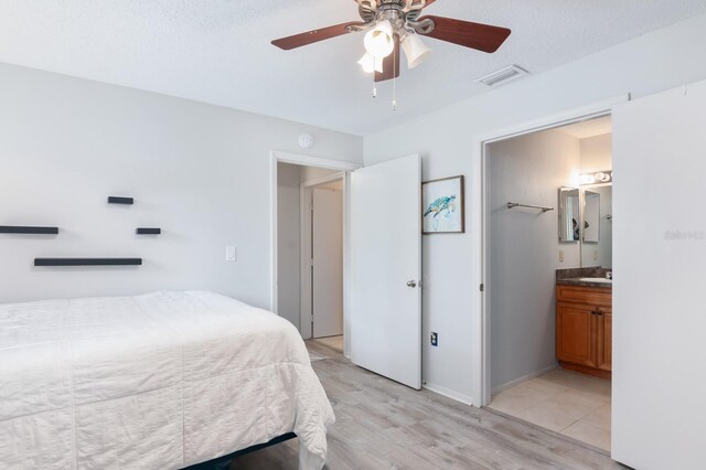 bedroom with ceiling fan, visible vents, light wood-style flooring, baseboards, and ensuite bathroom