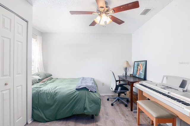 bedroom with a textured ceiling, ceiling fan, a closet, and light hardwood / wood-style flooring