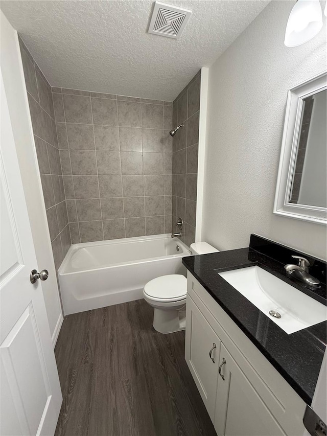 full bathroom featuring toilet, hardwood / wood-style flooring, tiled shower / bath, a textured ceiling, and vanity