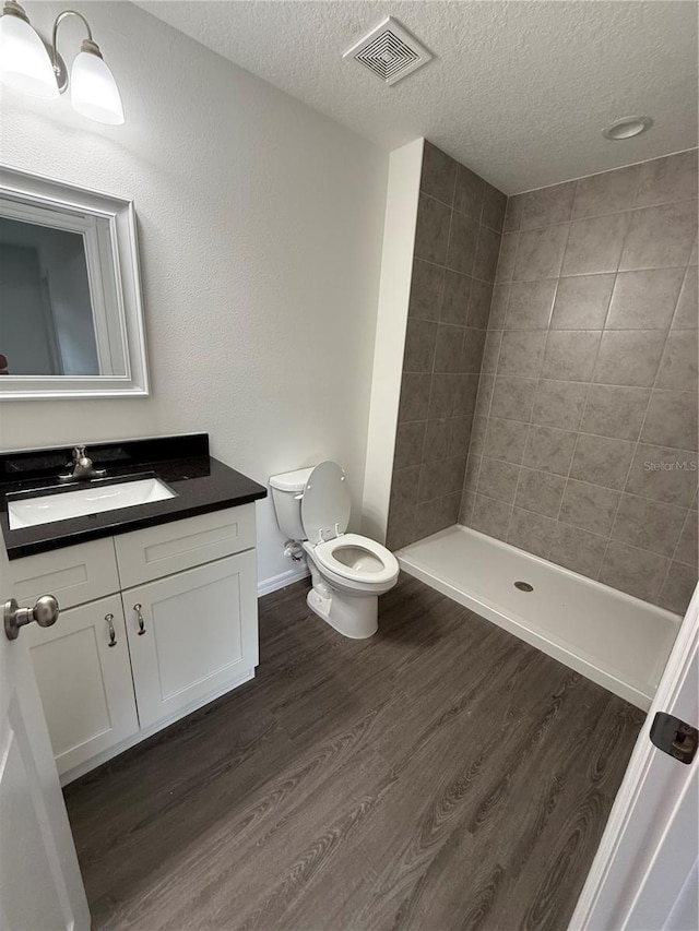 bathroom featuring a textured ceiling, wood-type flooring, vanity, toilet, and tiled shower