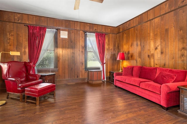 living room with ceiling fan, dark wood-type flooring, and wood walls