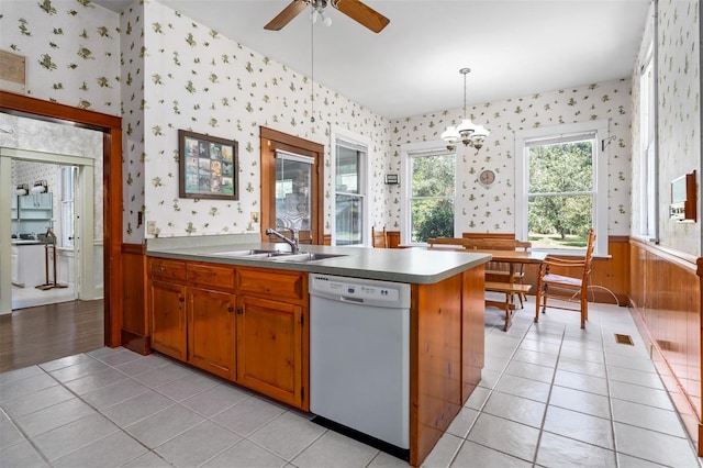 kitchen with wood walls, light tile patterned flooring, decorative light fixtures, sink, and dishwasher