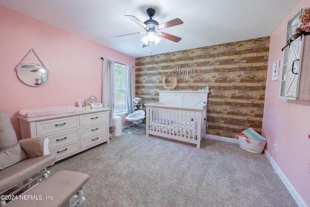 bedroom with a crib, wood walls, light carpet, and ceiling fan