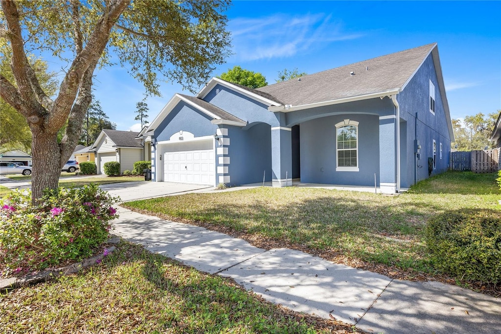 single story home with covered porch, a front yard, stucco siding, concrete driveway, and an attached garage