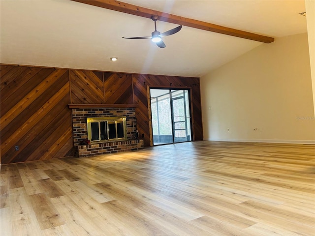 unfurnished living room featuring light hardwood / wood-style flooring, ceiling fan, a fireplace, lofted ceiling with beams, and wood walls