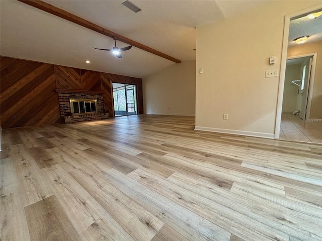 unfurnished living room with a fireplace, wood walls, vaulted ceiling with beams, ceiling fan, and light hardwood / wood-style flooring