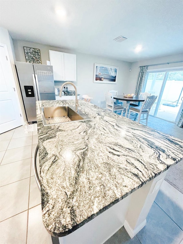 kitchen with stainless steel fridge, sink, light stone countertops, light tile patterned floors, and white cabinetry