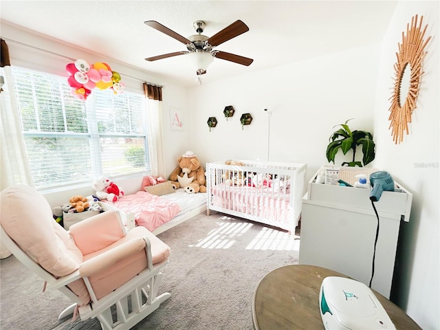 carpeted bedroom featuring a nursery area and ceiling fan