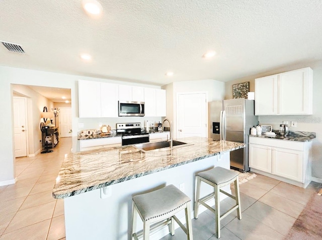 kitchen with a kitchen island with sink, stainless steel appliances, white cabinets, a breakfast bar, and sink