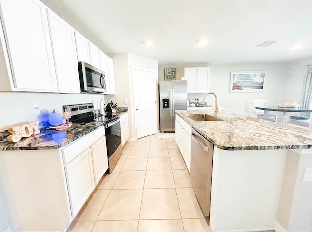 kitchen featuring dark stone countertops, sink, an island with sink, appliances with stainless steel finishes, and white cabinetry