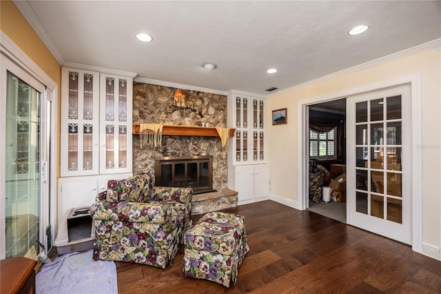 living room with crown molding, a healthy amount of sunlight, dark hardwood / wood-style flooring, and a stone fireplace