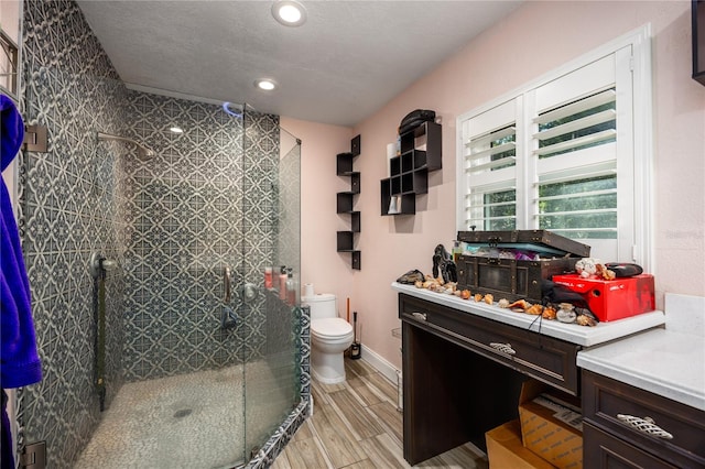 bathroom with a shower with door, vanity, a textured ceiling, and toilet