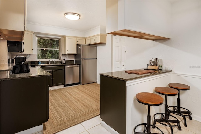 kitchen with sink, dark stone countertops, ornamental molding, appliances with stainless steel finishes, and cream cabinets