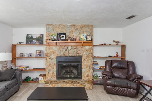 living room with light hardwood / wood-style flooring, a stone fireplace, and a textured ceiling