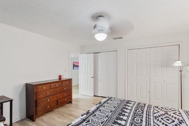 bedroom featuring light hardwood / wood-style flooring, two closets, and ceiling fan