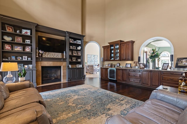 living room with a tiled fireplace, beverage cooler, dark wood-type flooring, and a high ceiling