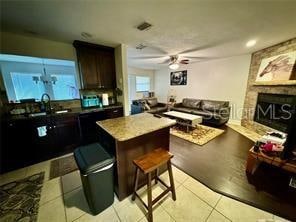 kitchen with sink, light tile patterned flooring, a large fireplace, dark brown cabinets, and ceiling fan