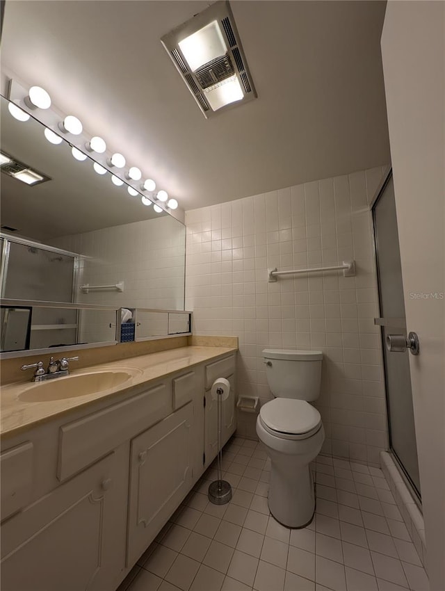 bathroom with a shower with door, tile walls, toilet, vanity, and tile patterned floors