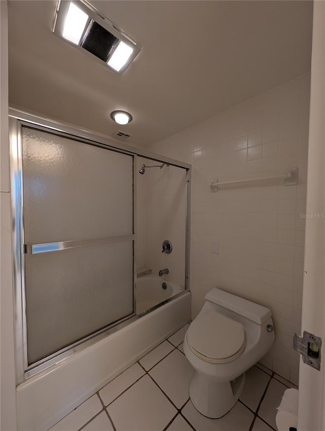 bathroom with toilet, bath / shower combo with glass door, tile patterned floors, and tile walls