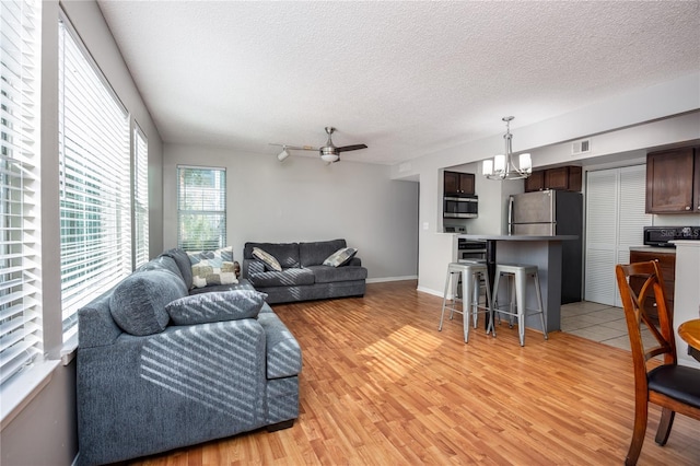 living room featuring light hardwood / wood-style floors, a textured ceiling, and ceiling fan with notable chandelier