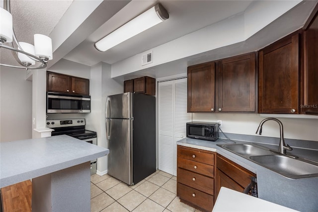 kitchen featuring dark brown cabinets, light tile patterned floors, appliances with stainless steel finishes, sink, and decorative light fixtures