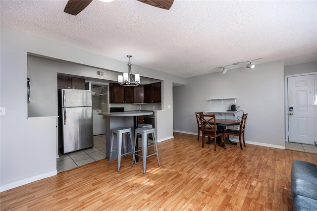 kitchen featuring stainless steel fridge, a kitchen breakfast bar, a textured ceiling, light hardwood / wood-style floors, and dark brown cabinetry