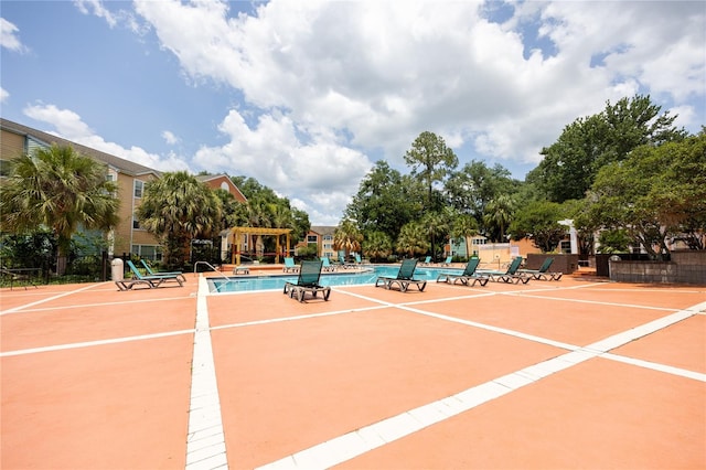 view of tennis court with a patio, a community pool, and basketball hoop