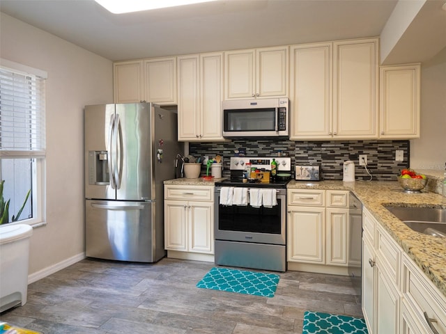 kitchen with cream cabinetry, light hardwood / wood-style flooring, stainless steel appliances, light stone counters, and tasteful backsplash