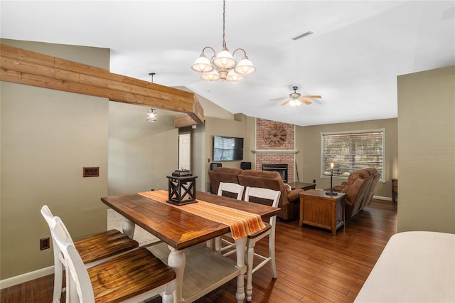 dining area with lofted ceiling, ceiling fan with notable chandelier, a brick fireplace, and dark hardwood / wood-style flooring