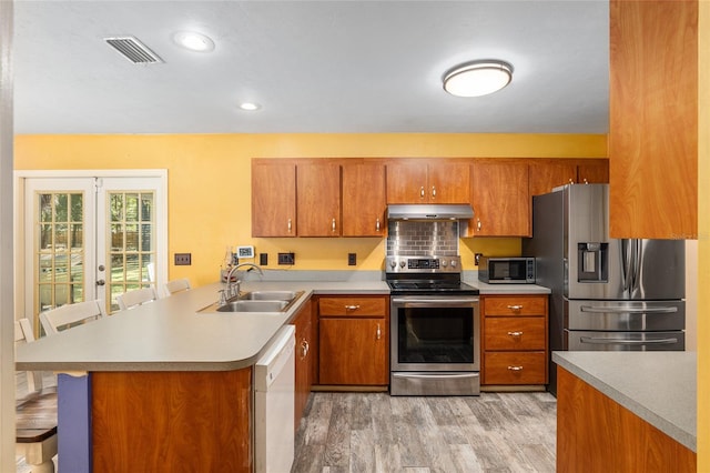 kitchen featuring kitchen peninsula, appliances with stainless steel finishes, a kitchen bar, light hardwood / wood-style floors, and sink