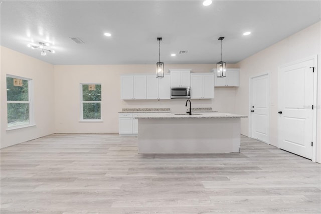 kitchen featuring white cabinetry, light hardwood / wood-style flooring, a center island with sink, and hanging light fixtures