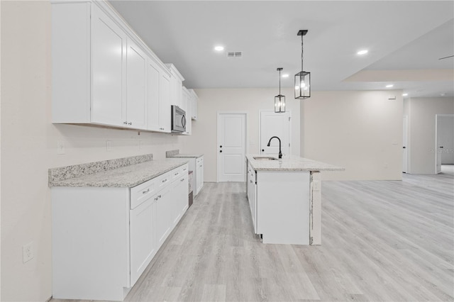 kitchen with white cabinets, a center island with sink, light hardwood / wood-style floors, decorative light fixtures, and sink